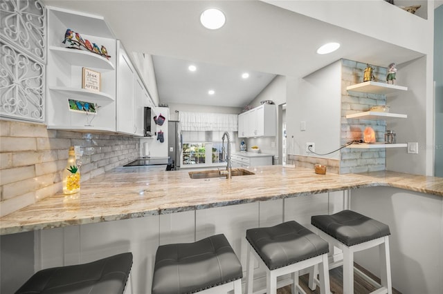 kitchen featuring light stone counters, white cabinetry, a breakfast bar area, and kitchen peninsula