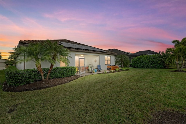 back house at dusk featuring a lawn and solar panels