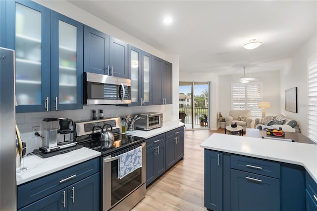 kitchen featuring ceiling fan, decorative backsplash, blue cabinets, light wood-type flooring, and stainless steel appliances