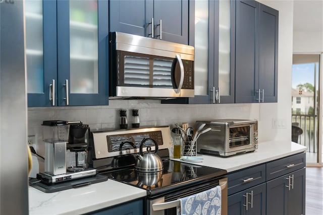 kitchen featuring backsplash, light stone counters, blue cabinetry, and appliances with stainless steel finishes