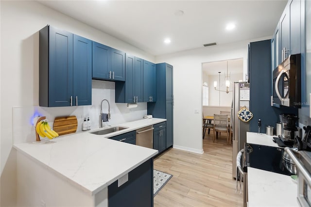 kitchen with kitchen peninsula, sink, blue cabinets, light hardwood / wood-style floors, and stainless steel appliances