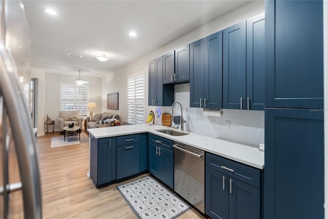 kitchen with kitchen peninsula, dishwasher, sink, blue cabinetry, and decorative backsplash