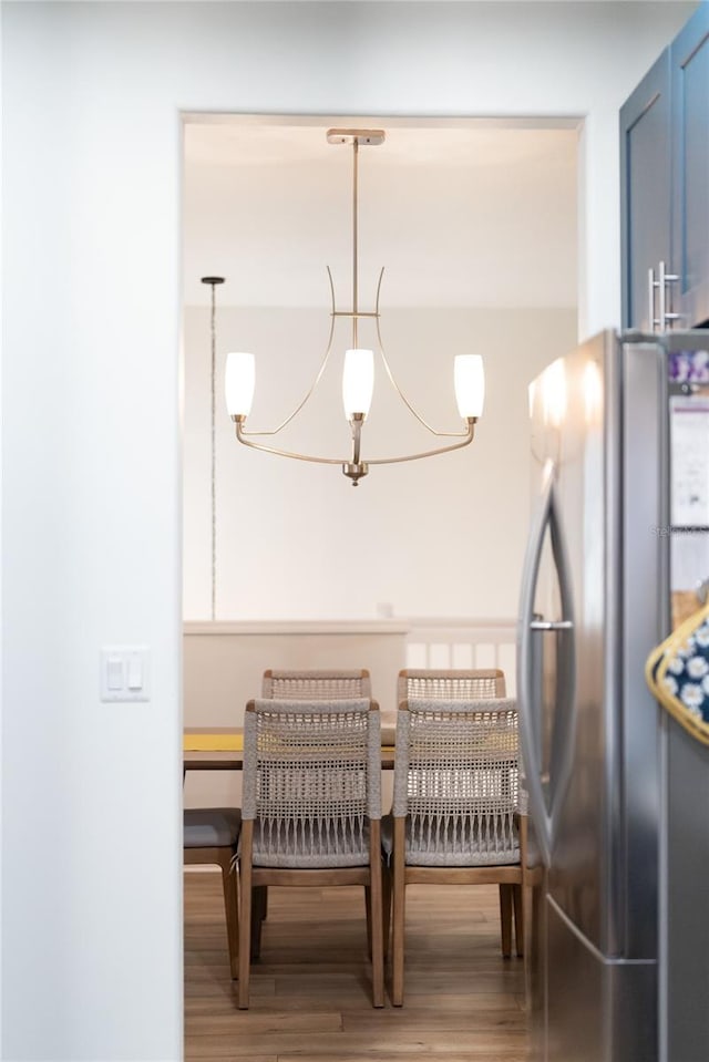 interior space with wood-type flooring, a chandelier, stainless steel fridge, and hanging light fixtures