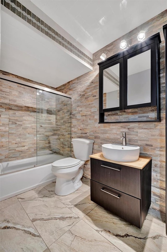 full bathroom with combined bath / shower with glass door, vanity, tile walls, and toilet