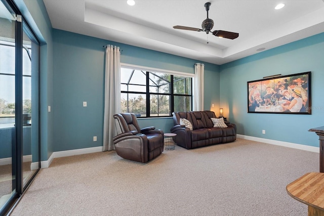 living area featuring ceiling fan, a tray ceiling, and carpet