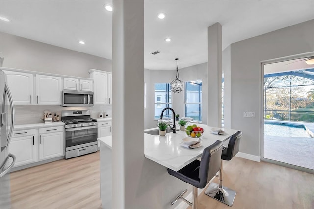 14146 Cattle Egret Pl, Bradenton, FL 34202 - kitchen with an inviting chandelier, light hardwood / wood-style flooring, hanging light fixtures, stainless steel appliances, and white cabinets