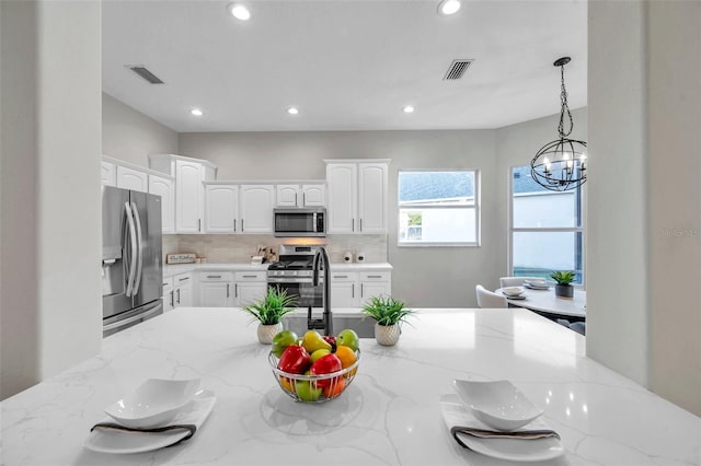 14146 Cattle Egret Pl, Bradenton, FL 34202 - kitchen featuring stainless steel appliances, a notable chandelier, white cabinets, hanging light fixtures, and light stone counters