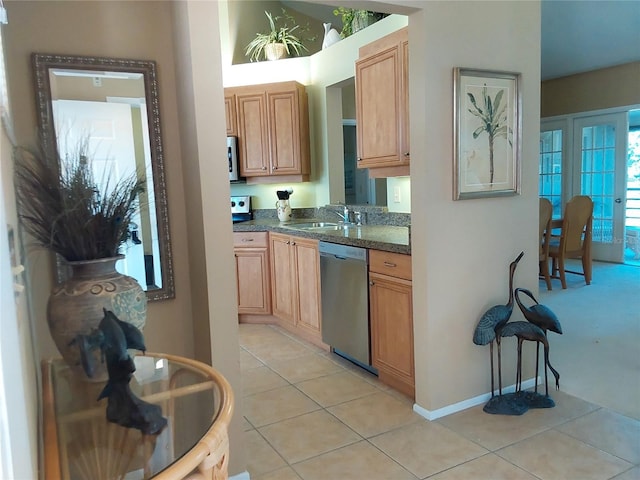 kitchen with light tile patterned floors, appliances with stainless steel finishes, dark stone countertops, and sink