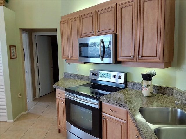 kitchen with stone counters, light tile patterned floors, stainless steel appliances, and sink