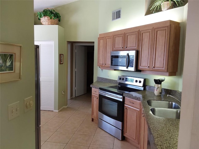 kitchen featuring light tile patterned floors, stainless steel appliances, dark stone countertops, a towering ceiling, and sink