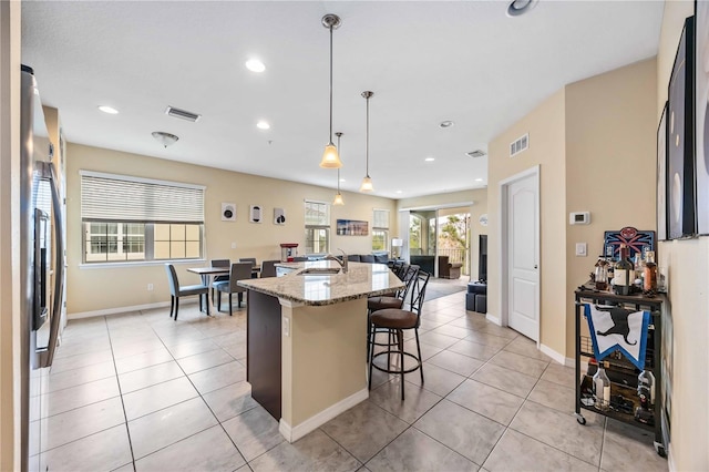 kitchen featuring sink, hanging light fixtures, a kitchen island with sink, a breakfast bar area, and light stone counters