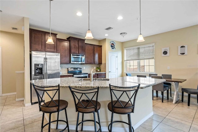 kitchen featuring stainless steel appliances, backsplash, a center island with sink, and hanging light fixtures