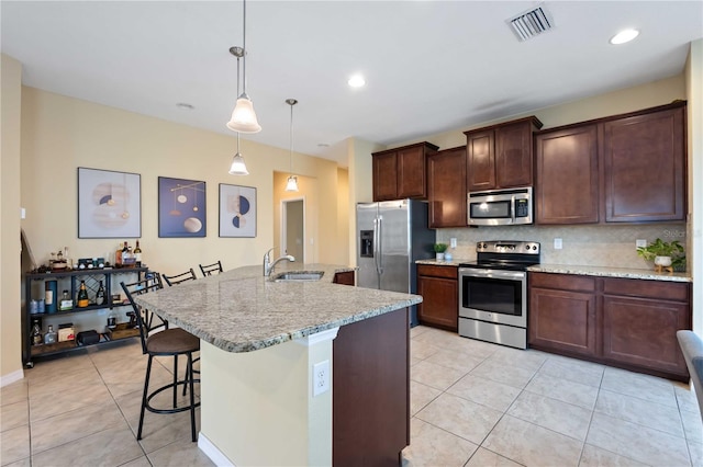 kitchen with pendant lighting, stainless steel appliances, sink, a kitchen island with sink, and a breakfast bar area