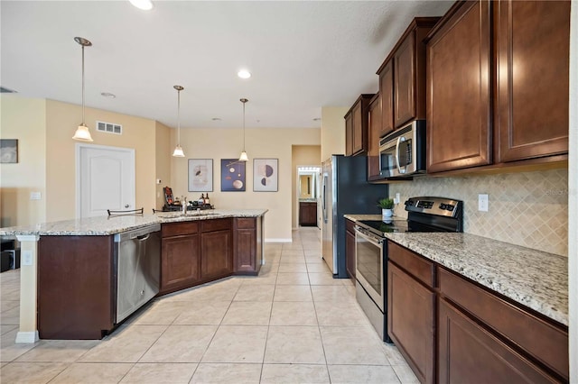 kitchen featuring light tile patterned floors, appliances with stainless steel finishes, pendant lighting, light stone counters, and sink