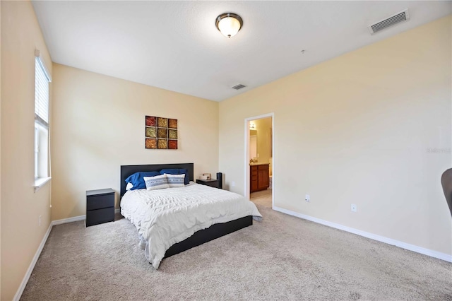 bedroom with ensuite bathroom and light carpet