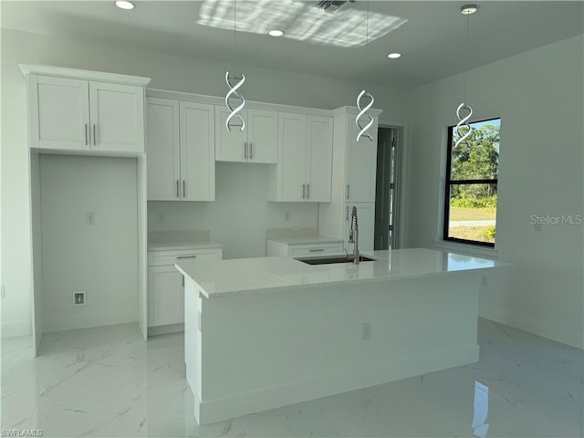 kitchen featuring sink, pendant lighting, white cabinets, and a kitchen island with sink