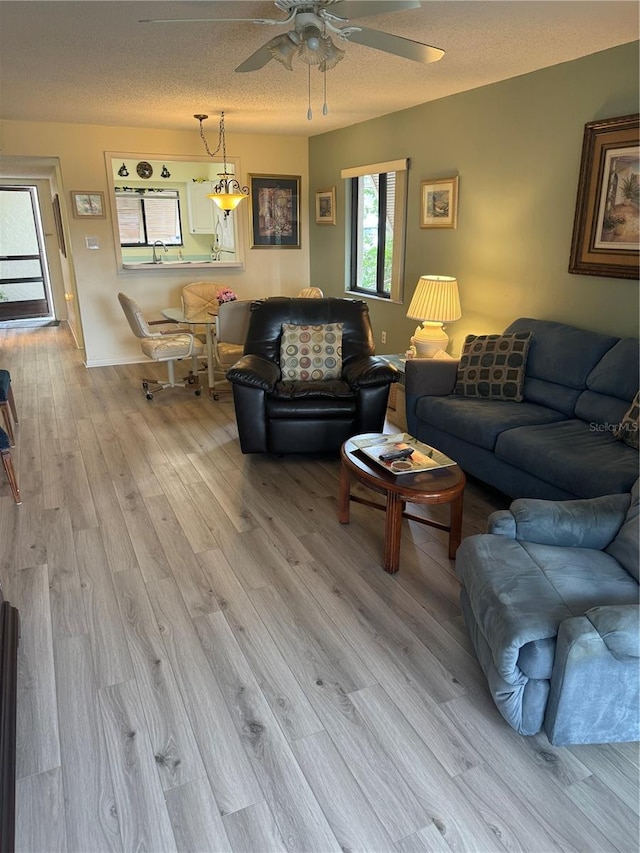 living room with a textured ceiling, ceiling fan, and light hardwood / wood-style flooring