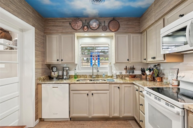 kitchen featuring light stone countertops, sink, white appliances, and cream cabinetry