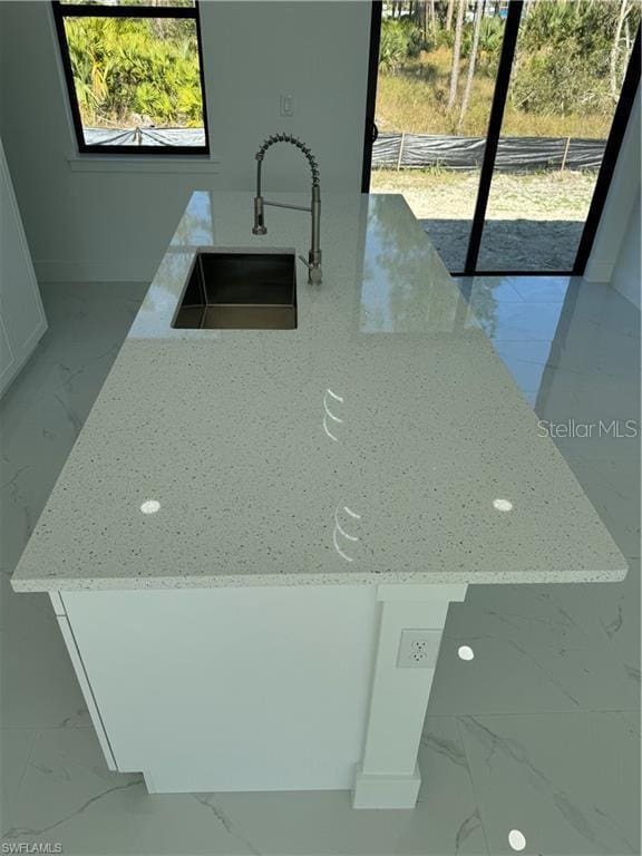 kitchen with light stone counters, a center island, sink, and white cabinets