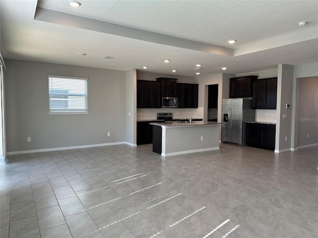 kitchen with a center island with sink, appliances with stainless steel finishes, a raised ceiling, tasteful backsplash, and sink