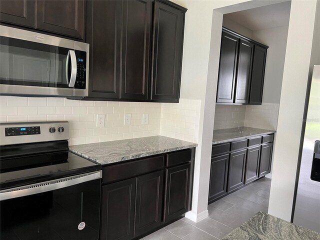 kitchen featuring light stone countertops, light tile patterned floors, backsplash, and appliances with stainless steel finishes