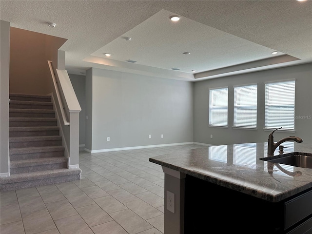 kitchen featuring a textured ceiling, sink, light tile patterned flooring, a tray ceiling, and a center island with sink