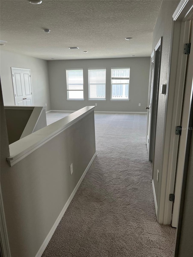 corridor featuring light colored carpet and a textured ceiling