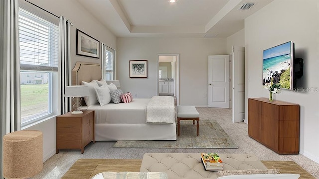 bedroom featuring light colored carpet, connected bathroom, and a raised ceiling