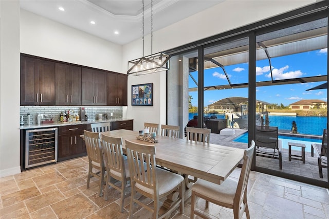 dining area featuring wine cooler, a water view, crown molding, and a towering ceiling