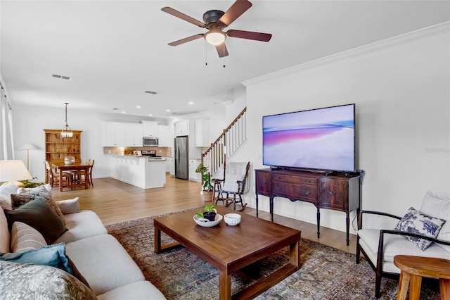 living room featuring ceiling fan, ornamental molding, and light hardwood / wood-style floors