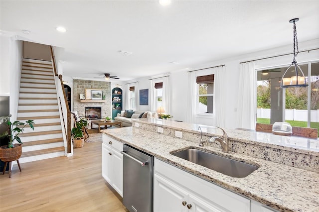 kitchen with stainless steel dishwasher, sink, hanging light fixtures, a stone fireplace, and white cabinets