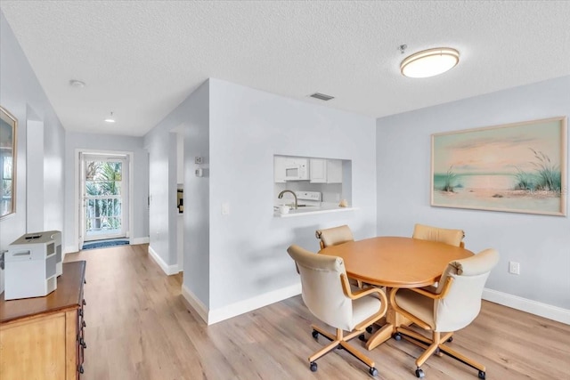 dining space with sink, a textured ceiling, and light hardwood / wood-style flooring