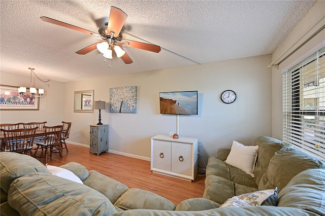 living room with ceiling fan with notable chandelier, a textured ceiling, and light wood-type flooring