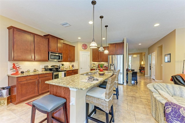 kitchen with sink, a kitchen island with sink, hanging light fixtures, stainless steel appliances, and a kitchen breakfast bar