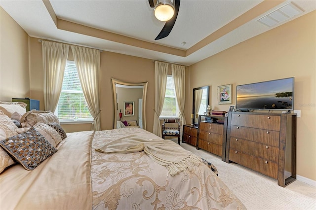 bedroom featuring light carpet, ceiling fan, and a tray ceiling