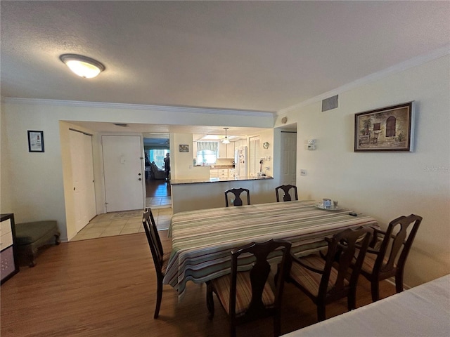 dining area with ceiling fan, a textured ceiling, ornamental molding, and light hardwood / wood-style floors