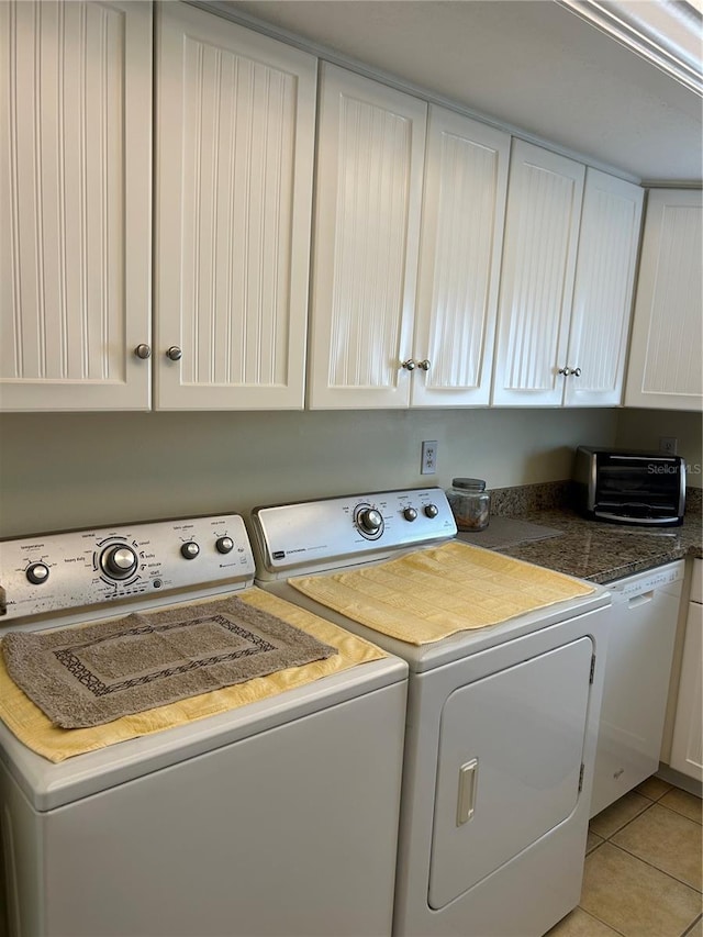 clothes washing area with washing machine and dryer, cabinets, and light tile patterned flooring