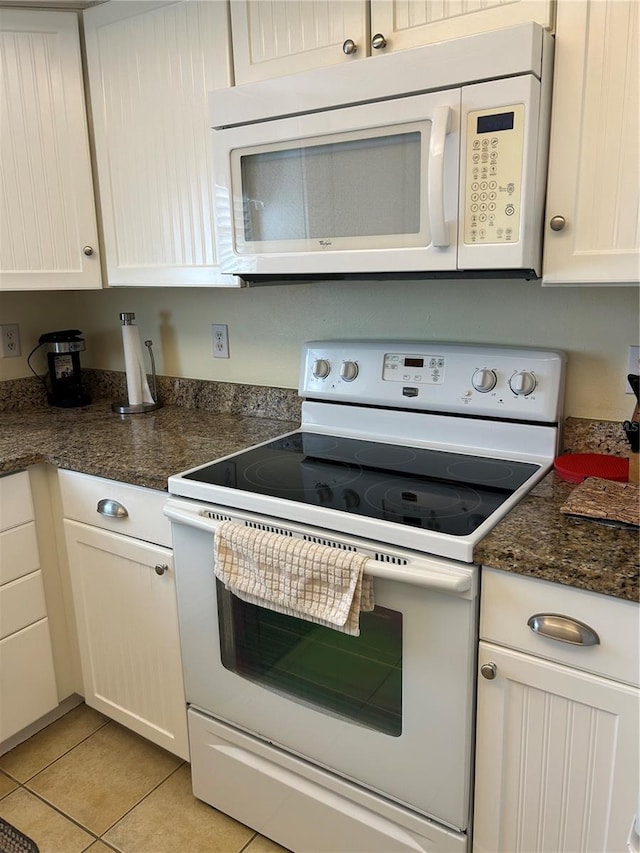 kitchen with light tile patterned floors, dark stone countertops, white appliances, and white cabinetry