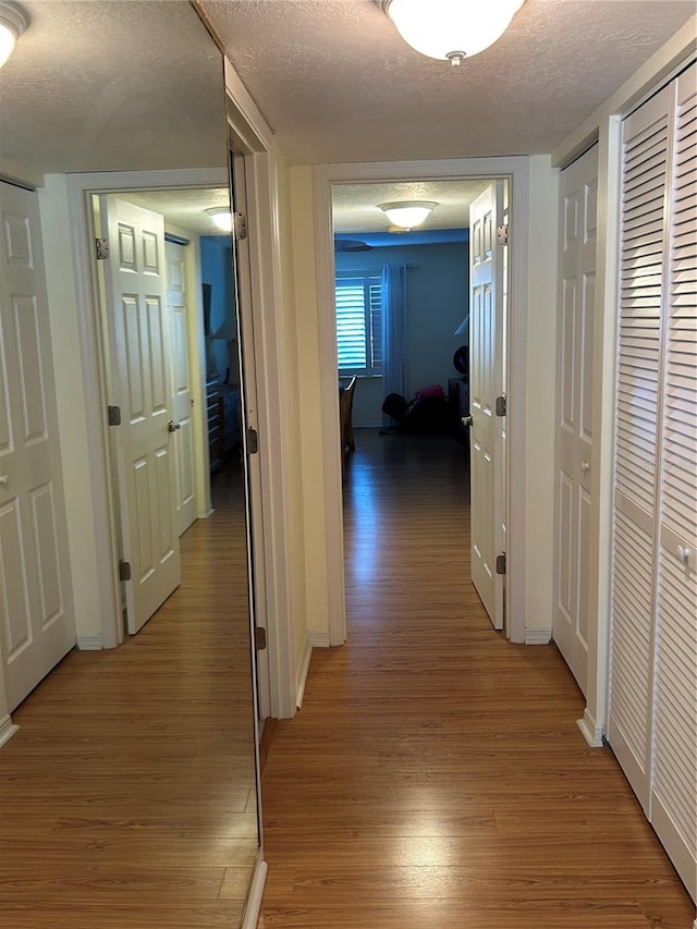 corridor with a textured ceiling and hardwood / wood-style floors