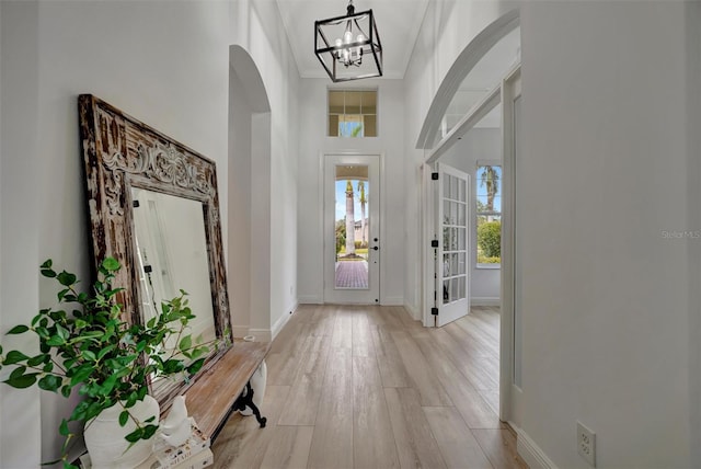 foyer entrance with light wood-type flooring, a notable chandelier, and a towering ceiling