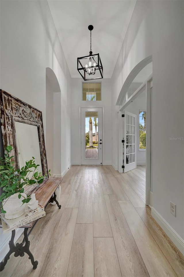 foyer with light wood-type flooring, a towering ceiling, and a notable chandelier