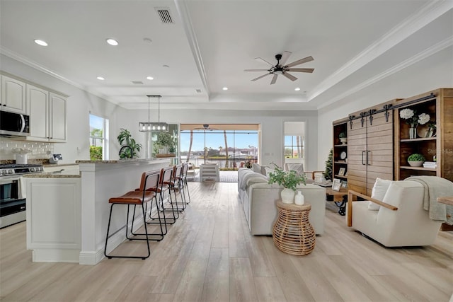 living room with light hardwood / wood-style floors, a barn door, ceiling fan, a raised ceiling, and ornamental molding