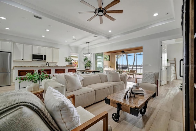 living room featuring light wood-type flooring, crown molding, and ceiling fan with notable chandelier