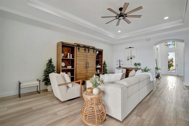 living room with light wood-type flooring, ceiling fan with notable chandelier, and a raised ceiling