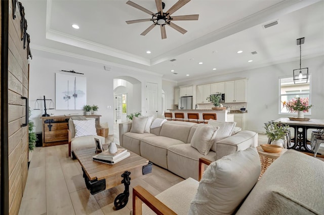 living room featuring ceiling fan, a healthy amount of sunlight, light hardwood / wood-style floors, and a raised ceiling