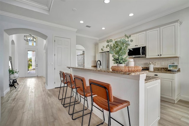 kitchen featuring white cabinets, a center island with sink, stainless steel appliances, and stone counters