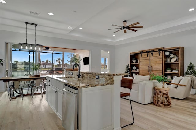 kitchen with decorative light fixtures, sink, a tray ceiling, white cabinetry, and an island with sink