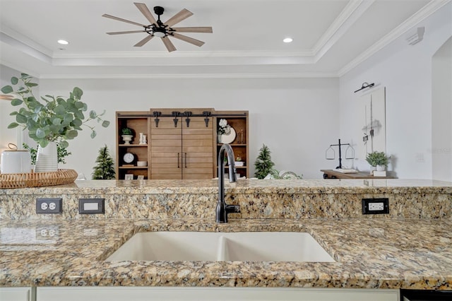 kitchen with ceiling fan, light stone counters, a tray ceiling, and sink