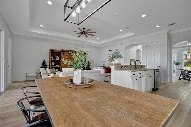 dining area with ceiling fan, a tray ceiling, and light wood-type flooring