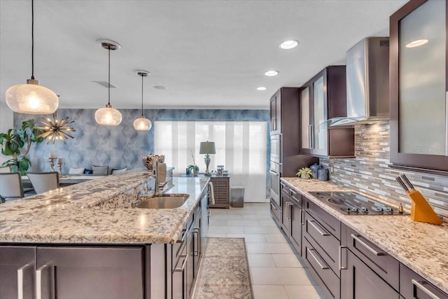 kitchen with sink, wall chimney range hood, black electric cooktop, and an island with sink